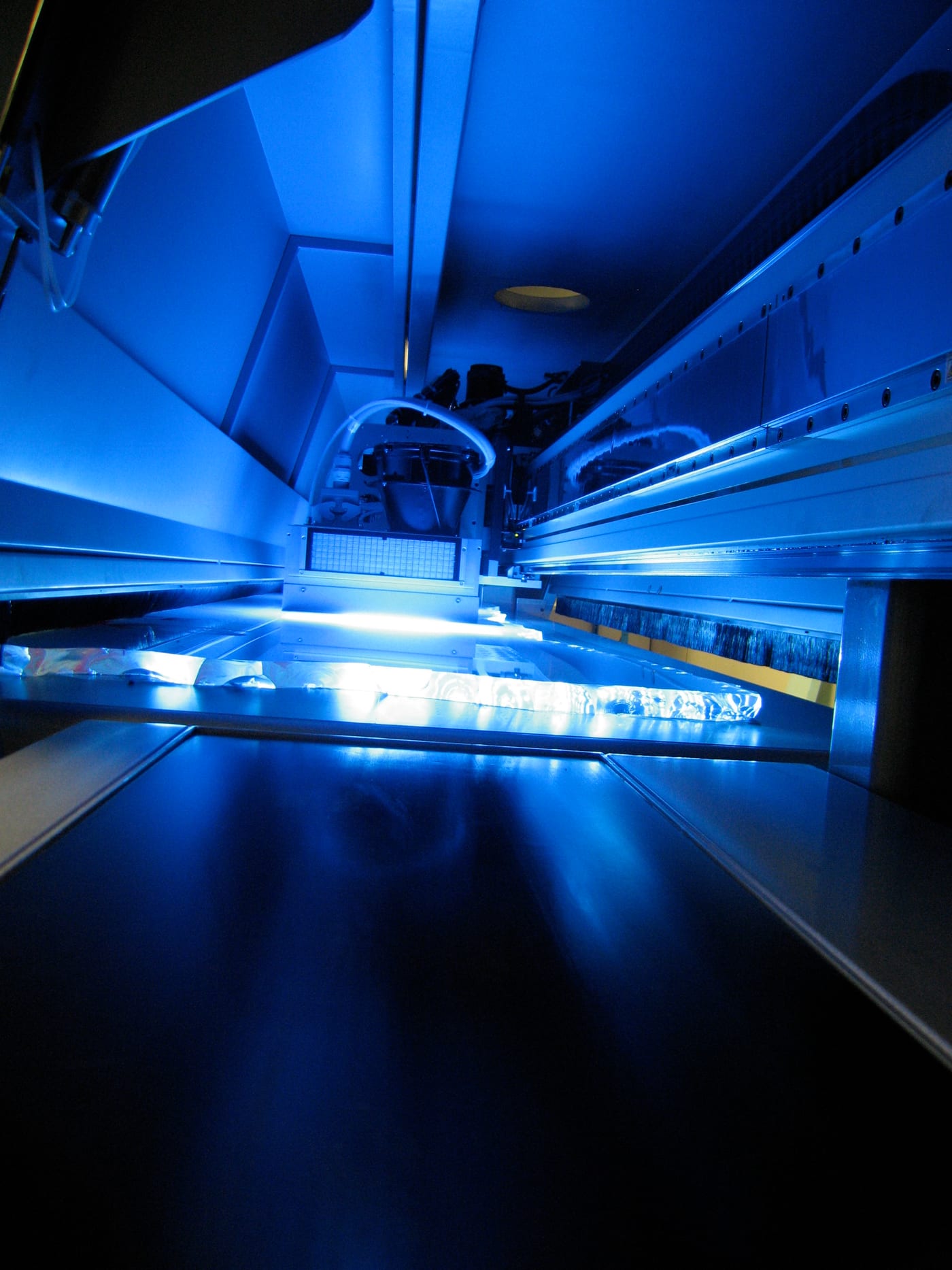 Inside a flatbed UV printer: the UV lamps light the carriage and the table, the ink cures instantly as they pass